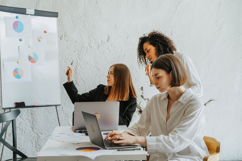 three individuals working on laptops in front of a whiteboard